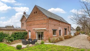 Une maison en briques avec un toit en pente, une porte d’entrée et un petit porche aménagé avec du mobilier d’extérieur.