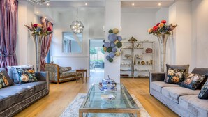 Un salon spacieux avec une table basse en verre, deux canapés ornés de coussins à motifs floraux et une étagère décorative où sont exposés divers objets.