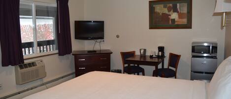 Una habitación de hotel con una cama grande, un televisor, una mesa de comedor con sillas, un microondas y un cuadro en la pared.