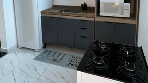 Una cocina compacta con un refrigerador blanco, un microondas en un estante y una estufa a gas.