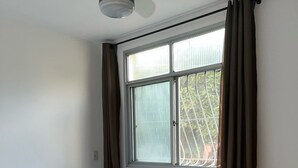 Un dormitorio con una cama, ventilador de techo, ventana con cortinas y vistas a zonas verdes.