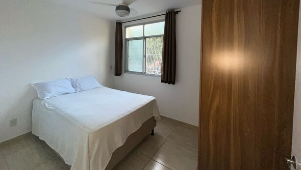 Un dormitorio con una cama, ventilador de techo, ventana con cortinas y una puerta de madera.