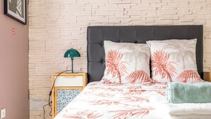 Una cama bien hecha con un edredón estampado con motivos de hojas tropicales, un cabecero oscuro y dos almohadas a juego.