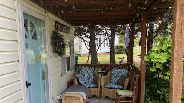 Eine überdachte Veranda mit Korbmöbeln, eine Tür mit Weihnachtskranz und ein Schild mit der Aufschrift 'NUNN COTTAGE'.