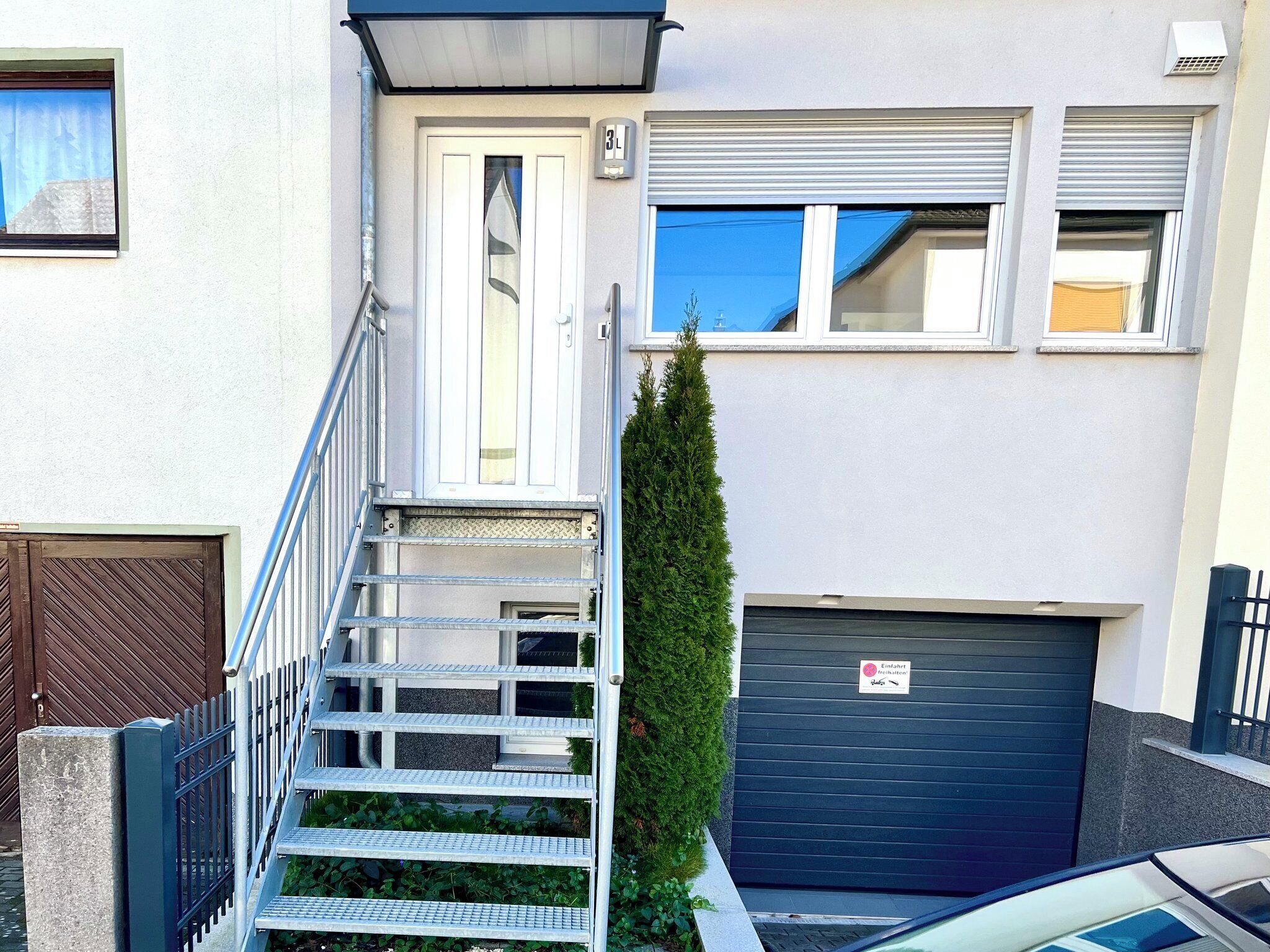 A residential building with a front door, a metal staircase, a garage, and a small tree.