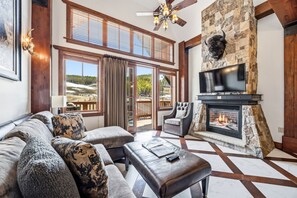 Una sala de estar con chimenea, televisor, sofá y vistas al exterior.
