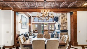 A dining area with a wooden table, upholstered chairs, a chandelier, and a stone wall.