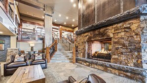 A spacious lobby with a stone fireplace, leather seating, a staircase, and a view of the upper floor.