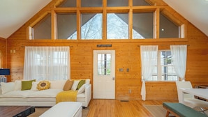 A cozy log cabin with a loft bedroom, a living area with a sofa and a bench, and a dining area. - Deer Haven Cabin, Stunning Mtn Views, Hot Tub+Fire Table+Grill, Game Room, WiFi! (Burnsville)