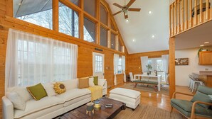 A spacious living room with a high ceiling and large windows, a wooden dining area, and a cozy seating arrangement. - Deer Haven Cabin, Stunning Mtn Views, Hot Tub+Fire Table+Grill, Game Room, WiFi! (Burnsville)