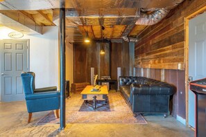 A room with a wooden ceiling, a blue chair, a black sofa, and a small table with a vase.
