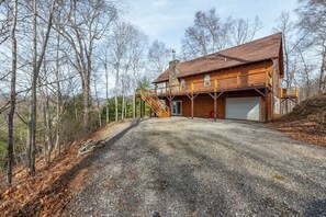 Eine zweistöckige Holzhütte mit einem Schotterweg, einer überdachten Veranda und einer Garage.