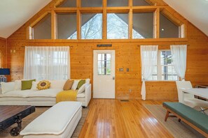 A log cabin interior with a loft bedroom, a living area with a sofa and a bench, and a dining area with a table and chairs.