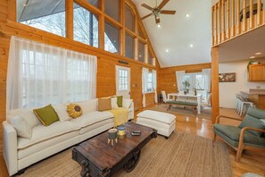 A spacious living area with a high ceiling, wooden beams, a sofa set, a coffee table, and a dining area.