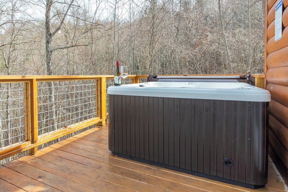 Un bain à remous sur une terrasse en bois, avec une rambarde en métal, entouré d’arbres.