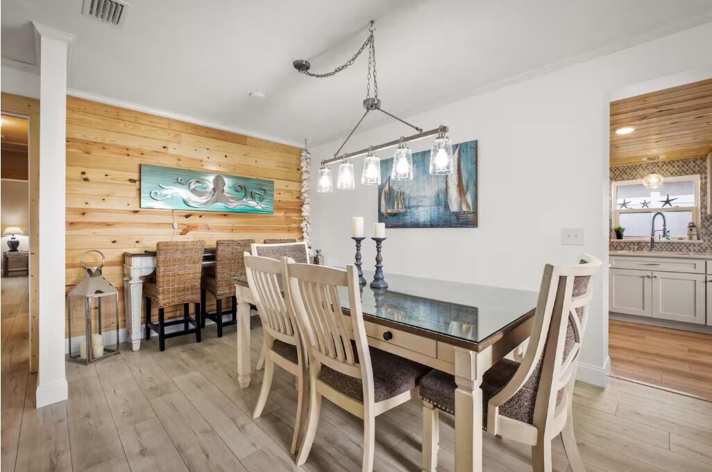 A dining area with a wooden wall, a glass table, and wicker chairs.