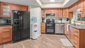 A modern kitchen with wooden cabinets, a black refrigerator, a water dispenser, a microwave, a stove, and a dishwasher. - Charming 3-bedroom house with Pool, WiFi and AC in amazing Mesa (Mesa)