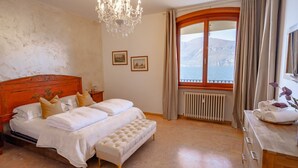 A bedroom with a large bed, a chandelier, a view of the sea, and a wooden headboard. - VILLA ESMERALDA BETH'S HOUSE (Brenzone sul Garda)