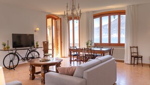 A living room with a sofa, a dining table, chairs, a TV, and a bicycle. - VILLA ESMERALDA BETH'S HOUSE (Brenzone sul Garda)