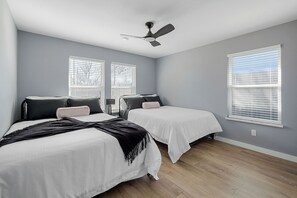 A bedroom with two beds, a ceiling fan, and large windows with blinds.