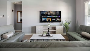 Ein modernes Wohnzimmer mit einem großen Flachbildfernseher an der Wand, einem Holzkonsolentisch mit dekorativen Pflanzen und zwei Sofas.