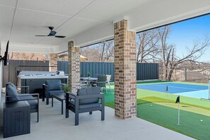 A covered patio area with outdoor seating, a grill, and a tennis court.