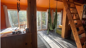 A room with a wooden ladder, a hammock, and a table with a chair. - Dragon’s Nest on River. Quiet Get-away (Tweed)
