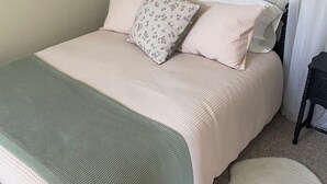 Una cama bien hecha con un edredón verde, dos almohadas y una almohada blanca con estampado floral.