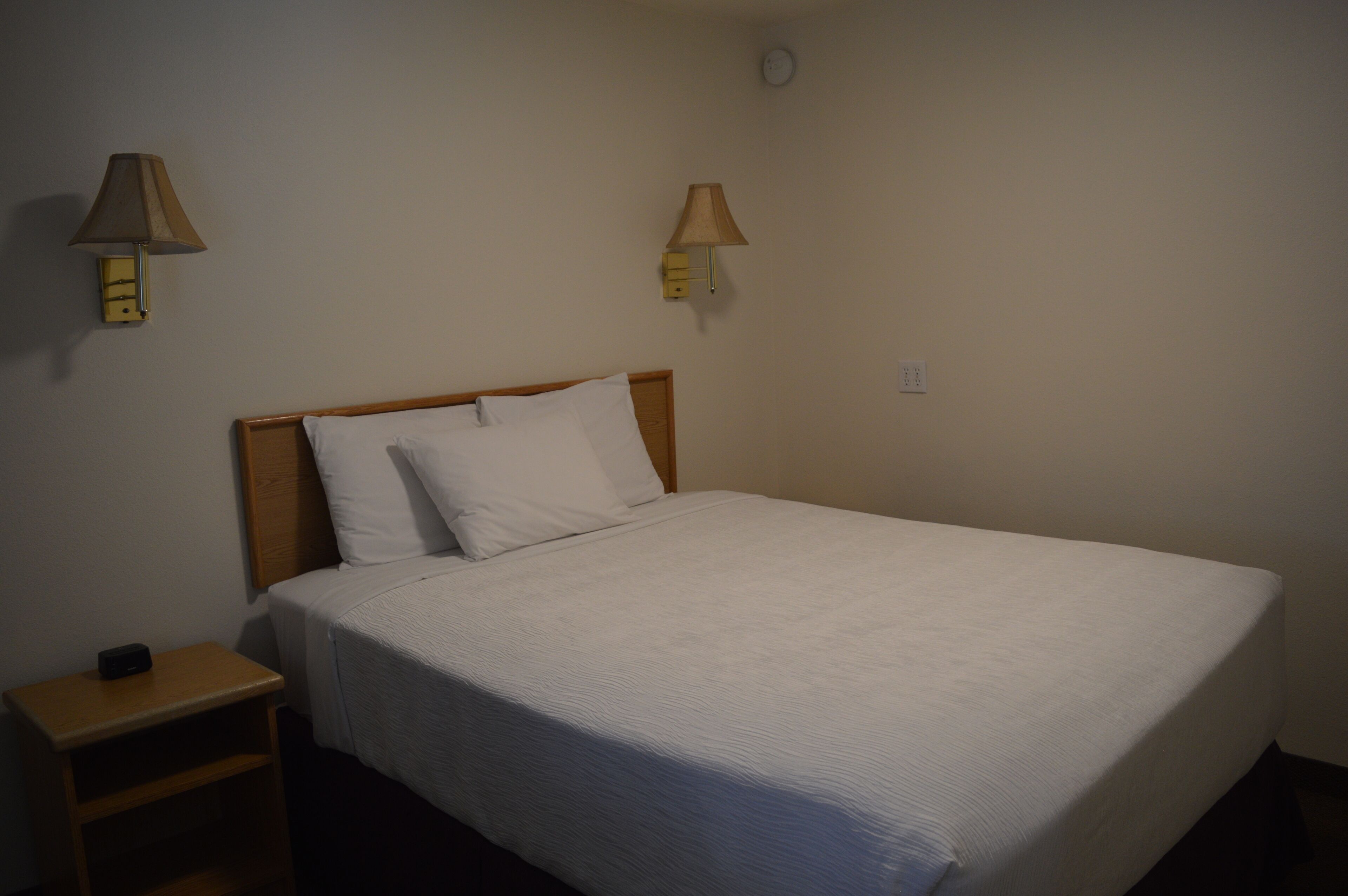 A single bed with a wooden headboard, two bedside lamps, and a nightstand with a clock.