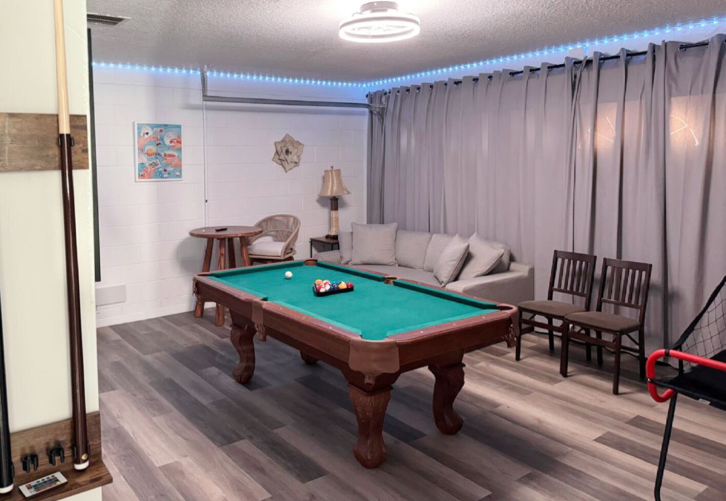 A pool table in a room with a sofa, chairs, and a lamp.