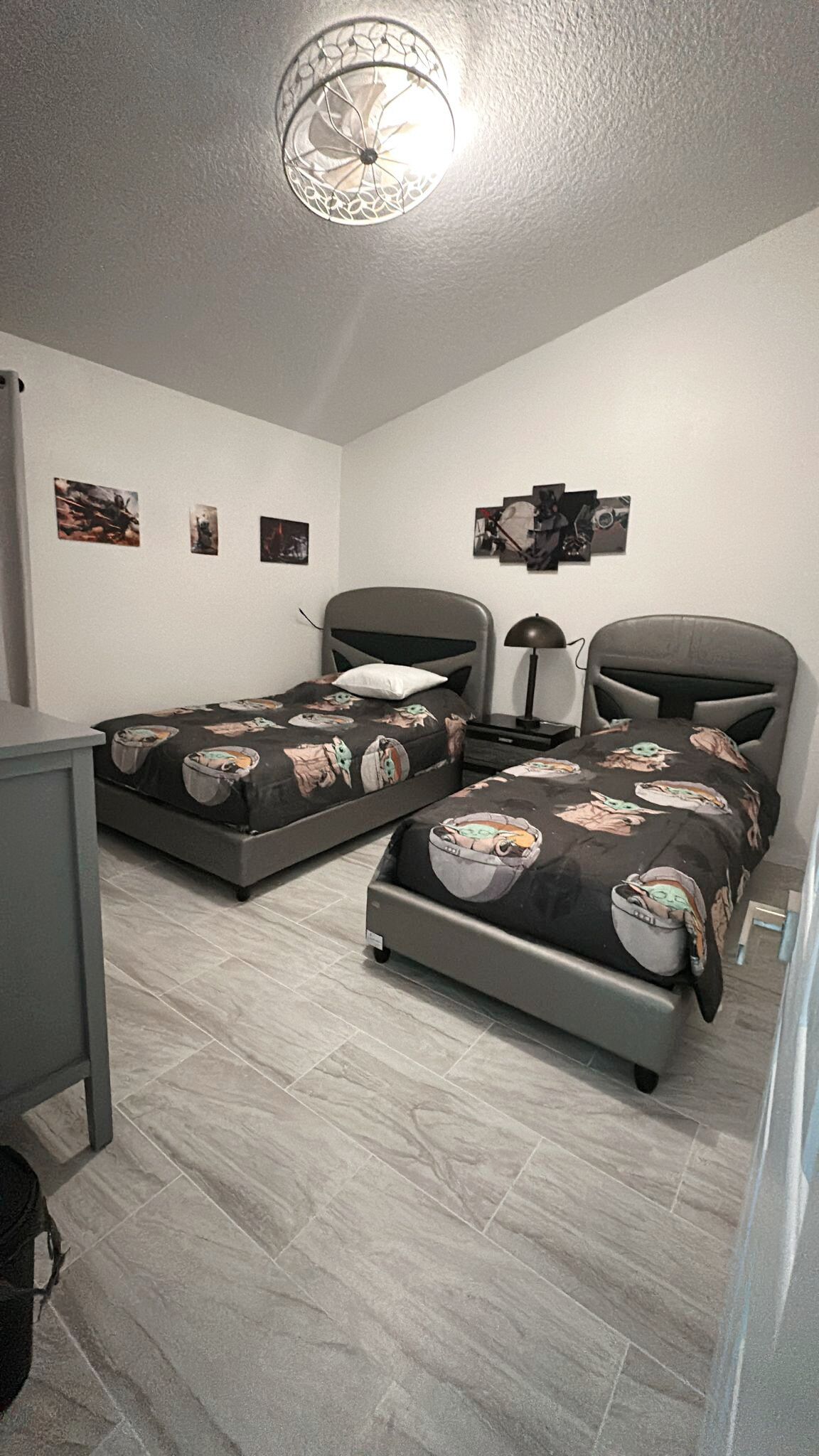 A bedroom with two beds, a desk, a chair, and a ceiling light fixture.