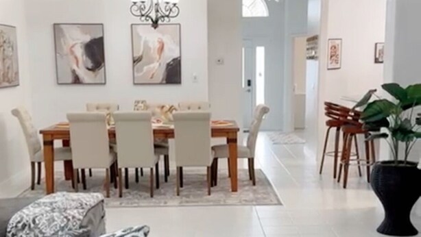 Ein modernes Wohnzimmer mit grauem Sofa, einer Essecke mit Holztisch und Stühlen sowie einer großen Topfpflanze.