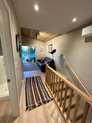 Un pasillo con una escalera de madera, una alfombra estampada y un sofá al fondo.