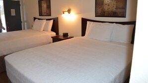 Una habitación de hotel con dos camas individuales, una mesita de noche con lámpara y un cuadro en la pared.