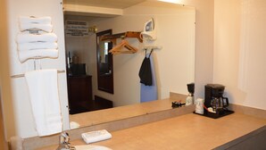 Un baño con lavamanos, espejo, perchero para toallas y cafetera.