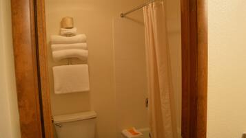 Un baño con inodoro, toallero con toallas dobladas y cortina de ducha.