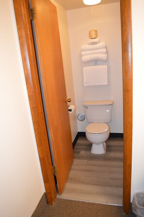 Un baño con puerta de madera, inodoro y toallero con toallas.