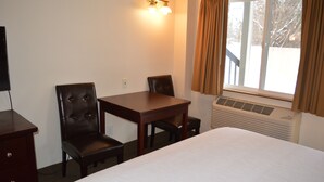 Habitación de hotel con cama, una mesa de madera, dos sillas, televisión y ventana con cortinas.