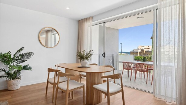 Un comedor moderno con una mesa redonda de madera y cuatro sillas, una planta en maceta y un espejo redondo en la pared.