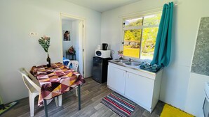 A compact kitchen with a dining table, a refrigerator, a microwave, and a window with curtains. - FARE HIRO BUNGALOW 1 SEASIDE (Moorea-Maiao)