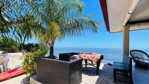 A covered outdoor seating area with wicker furniture and a table, overlooking a calm sea. - FARE HIRO BUNGALOW 1 SEASIDE (Moorea-Maiao)