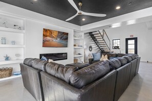 A modern living room with a large sectional sofa, a flat-screen TV, and a staircase leading to an upper level.