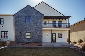 A two-story building with a stone facade, a balcony with outdoor seating, and a clear sky. - Zion's Sunset is BRAND NEW!!! Beautiful courtyard, fun game room, roof top deck (Hurricane)