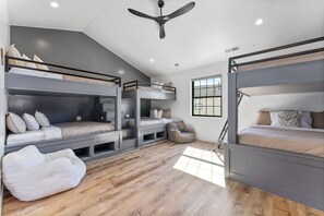 A modern, multi-level bunk bed room with a wooden floor, a ceiling fan, and a window providing natural light.