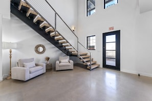 A spacious living area with a modern staircase, a sofa, a lamp, and a decorative mirror.