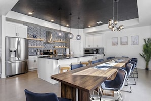 A modern kitchen with a central island, stainless steel appliances, and a dining area with a long wooden table and blue chairs.