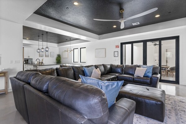 A spacious living area with a large sectional sofa, a ceiling fan, and a kitchen in the background.