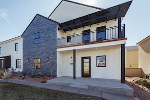 A modern two-story house with a stone facade, a balcony with black railings, and a small front porch.
