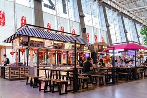 Un patio de comidas interior con varias mesas y puestos, rodeado de amplios ventanales.