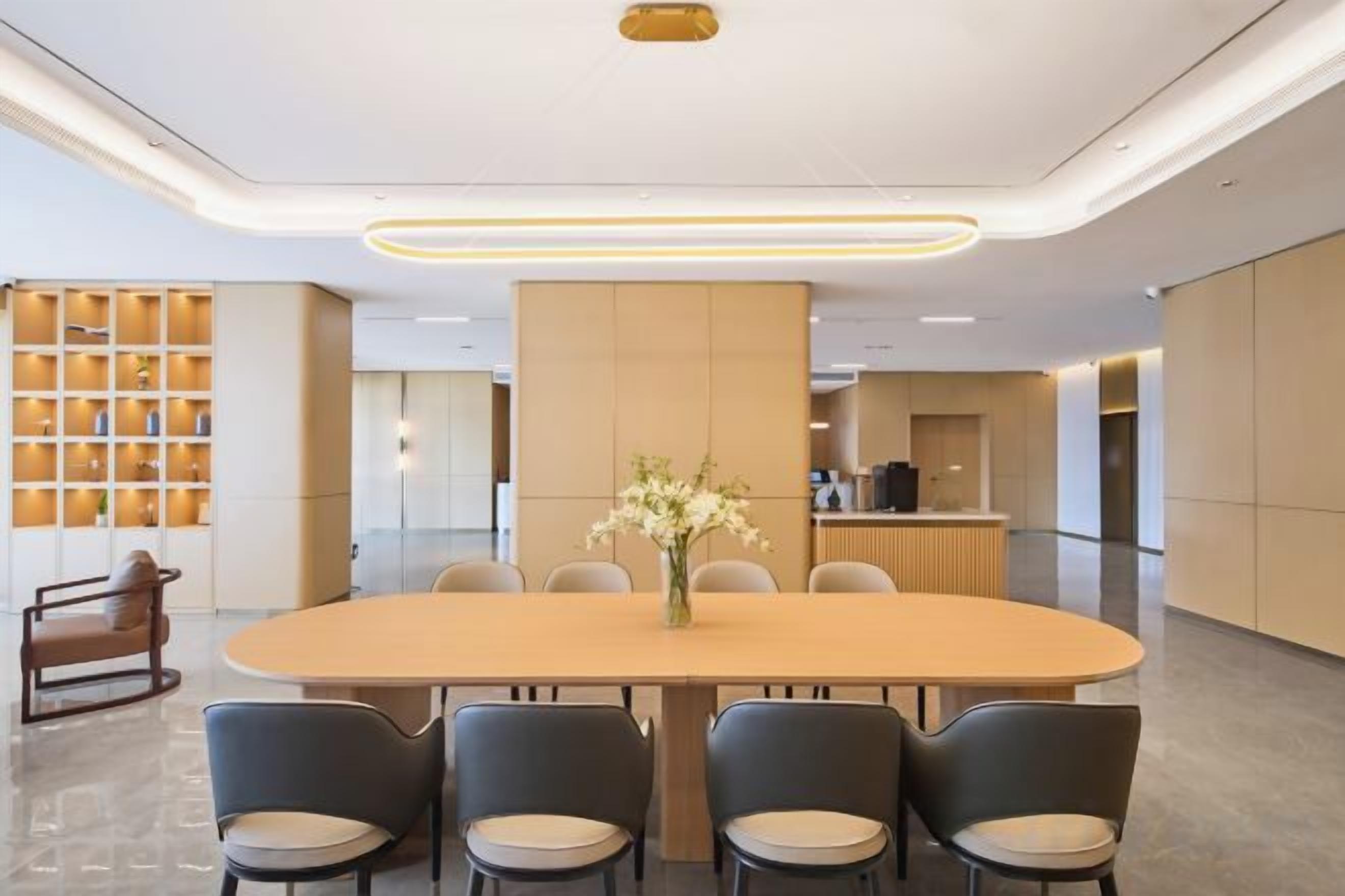 A modern conference room with a large oval table, six chairs, and a vase of flowers.